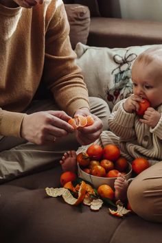 a baby sitting on the floor with oranges in it's mouth and an adult holding one