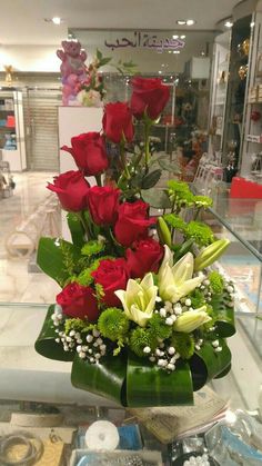 red roses and white lilies in a vase on display at a flower shop,