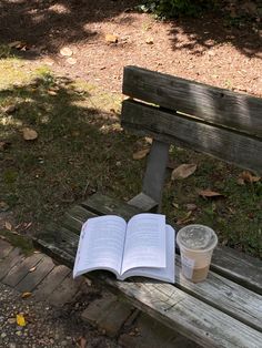 an open book sitting on top of a wooden bench next to a cup of coffee