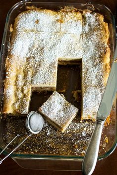 a cake with powdered sugar on top in a glass dish next to a knife and spoon