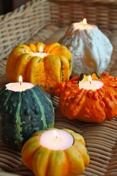 pumpkins and gourds are sitting on a wicker table with candles in them