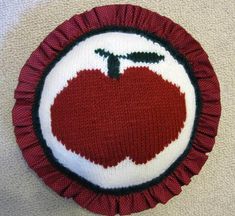 Apple for the teacher.  Hand knitted intarsia (picture knitting) techinque.  Original apple design hand knitted with acrylic yarn for front and back.   The ruffle is made out of cotton fabric in a dark red to go with the red apple.  Lined with cotton and lightly stuffed with poly fil. 14 inch diameter round. Spot clean. Hand made in a pet and smoke free environment. FREE SHIPPING Apple Knitting Pattern, Tapestry Crochet Apple, Embroidery Apple, Apple Crochet Coaster, Apple Core Quilt, Teacher Apple, Apple Design, Red Apple, Dark Red