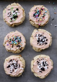 six cookies with frosting and sprinkles on a baking sheet covered in confetti