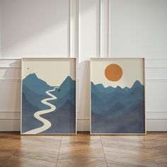 two framed art prints with mountains and a river in the middle, against a white wall