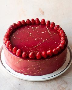 a red cake with raspberries on top is sitting on a white platter