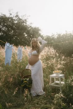 a pregnant woman standing in a field with clothes hanging on a line above her head