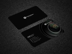 a black business card with a camera lens on the front and bottom, sitting on a dark surface