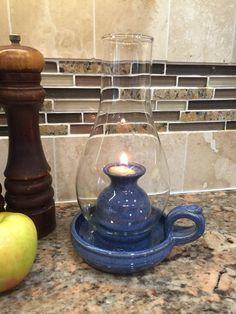 an apple sits on the counter next to a glass teapot and candle holder,