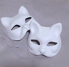 two white masks sitting on top of a gray cloth covered table next to each other