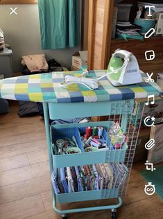 an ironing board sitting on top of a blue cart filled with cloths and other items