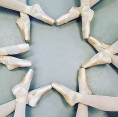 several pairs of ballet shoes arranged in a star shape on a gray surface with white tights