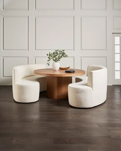 a round table with two chairs and a vase on it in front of a white paneled wall