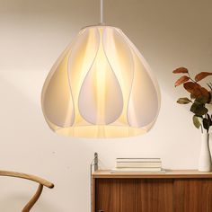 a white lamp hanging over a wooden table next to a vase with flowers in it