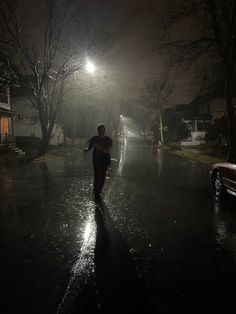 a man is walking down the street at night in the rain with his skateboard