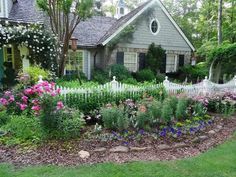 a white picket fence in front of a house with pink and purple flowers around it