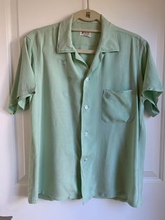 Vintage 1960s pale green, light-weight button-up, collared, short-sleeved shirt with breast pocket and subtle crest details on chest and pocket. Slight tear on back of left shoulder. Should be easy to fix. Also very faint discoloration on back. Both are pictured. I've reduced the price to reflect the damage. Classic Green Camp Shirt With Button Closure, Classic Green Collared Short Sleeve Shirt, Classic Green Short Sleeve Shirt, Green Button-up Camp Shirt With Pockets, Green Classic Short Sleeve Shirt With Camp Collar, Classic Green Short Sleeve Shirt With Camp Collar, Green Collared Short Sleeve Shirt With Buttons, Vintage Green Button-up Shirt, Vintage Solid Color Short Sleeve Shirt