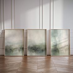 three framed paintings sitting on top of a wooden floor