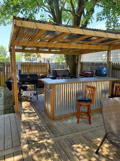 an outdoor kitchen area with grill, bar and chairs on the deck under a tree