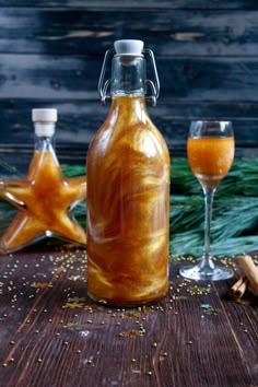 a glass bottle filled with liquid next to two wine glasses on a wooden table and pine branches