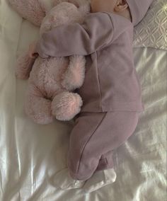 a baby sleeping with a stuffed animal on top of it's back in a bed