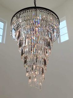 a chandelier hanging from the ceiling in a room with two windows behind it