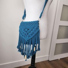 a mannequin wearing a blue crocheted bag with tassels on it