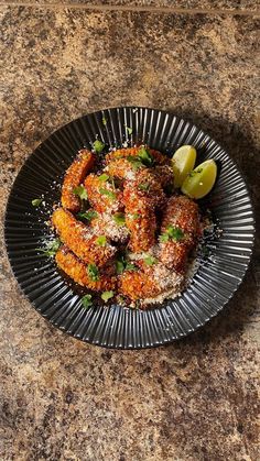 a black plate topped with fried food next to a lemon wedge on top of a table