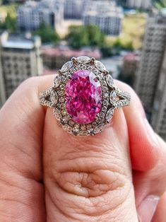 a woman's hand holding a ring with a pink stone in the center and white diamonds surrounding it