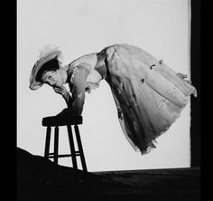 a black and white photo of a woman leaning on a stool with her legs spread out