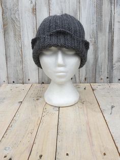 a white mannequin head wearing a gray knitted hat on top of a wooden table