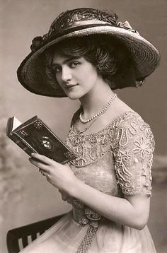 an old black and white photo of a woman wearing a hat holding a book in her hands