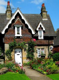 a house with flowers and plants around it's front door, on a sunny day