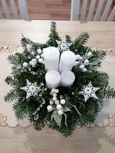 a bouquet of white candles and greenery on top of a wooden table with snowflakes