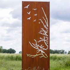 a tall metal sign sitting in the middle of a grass covered field with birds flying over it