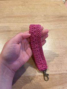 a hand holding a pink crochet keychain on top of a wooden table