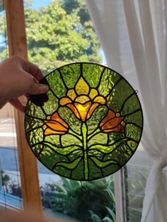 a hand holding up a stained glass flower in front of a window with white curtains