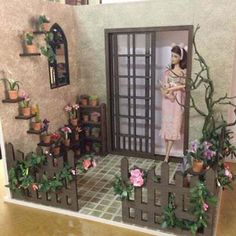 a doll is standing in the doorway of a house with potted plants and flowers