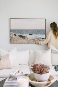 a woman standing on the edge of a couch in front of a painting and coffee table