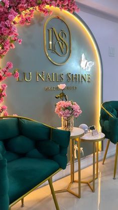 the interior of a nail salon with green chairs and pink flowers on the wall behind them