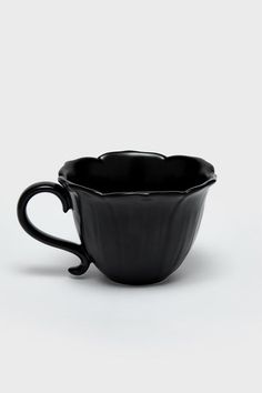 a black coffee cup sitting on top of a white table