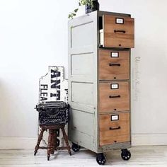 an old filing cabinet next to a plant on top of a wooden stool in front of a white wall