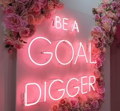 a neon sign that says be a goal digger surrounded by pink flowers and greenery