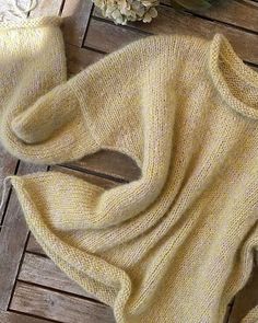 a yellow sweater laying on top of a wooden floor next to a vase with flowers