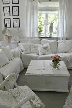 a living room filled with white furniture and pictures on the wall above it's windows