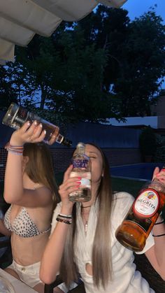 two women in bikinis drinking from bottles at an outdoor bar with trees in the background