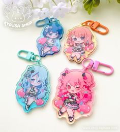 four keychains with anime characters on them sitting next to flowers and paper clips