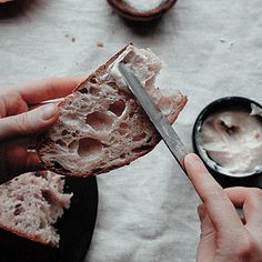 a person holding a piece of bread with cream cheese on it and a knife in their hand