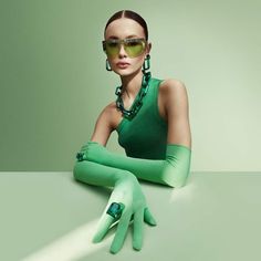 a woman wearing green gloves and sunglasses sitting on a table with her hands folded out