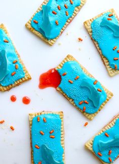 some cookies with blue icing and orange sprinkles on a white surface