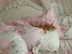 an orange cat laying on top of a bed covered in pink and white sheets with ruffles